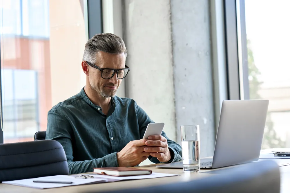 man looking at smartphone while working on laptop