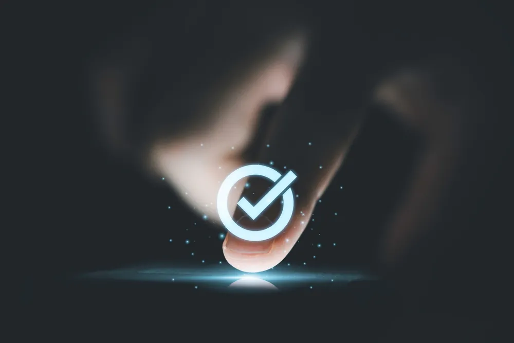 finger pushing button on cell phone with check mark on top