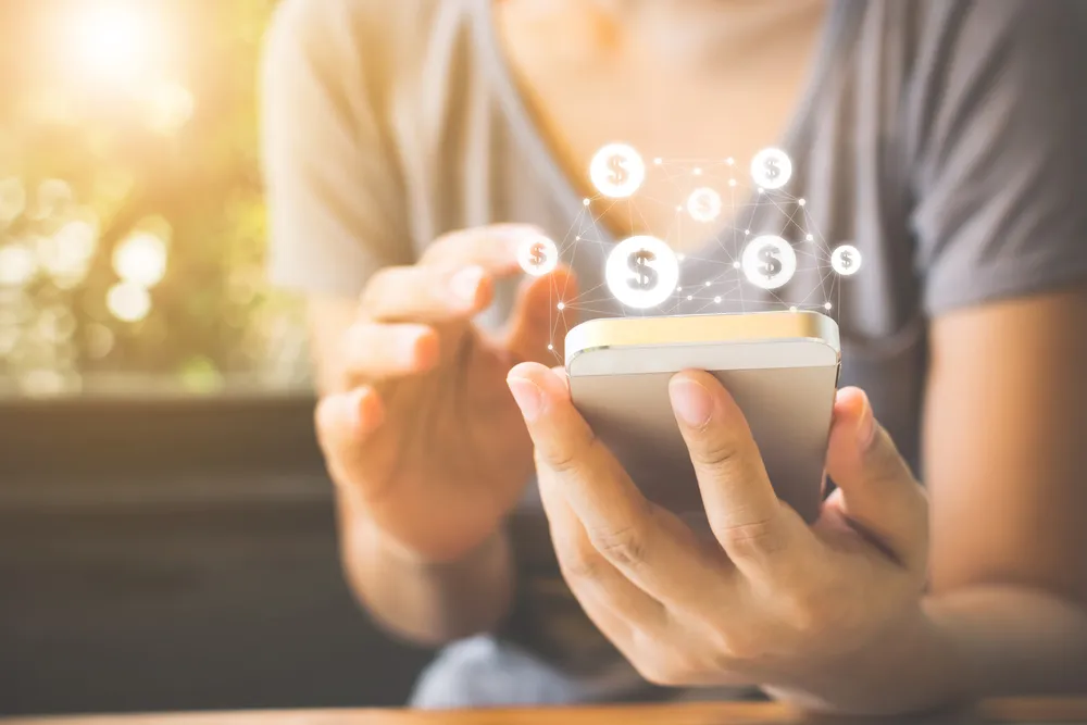 Person's torso holding a mobile phone surrounded by dollar signs