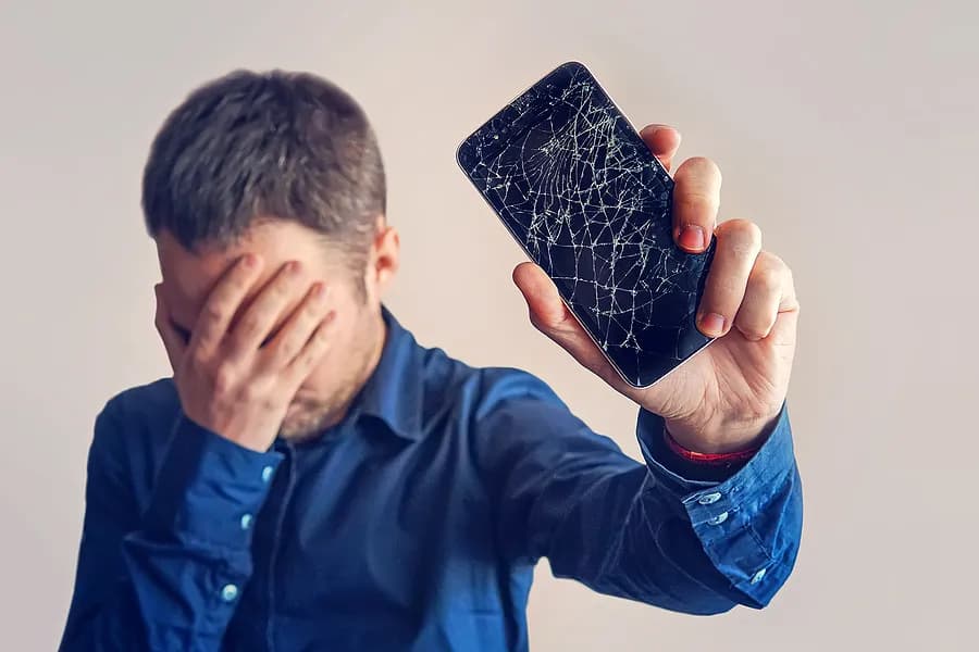 A man covering his eyes and holding a mobile phone away from himself.