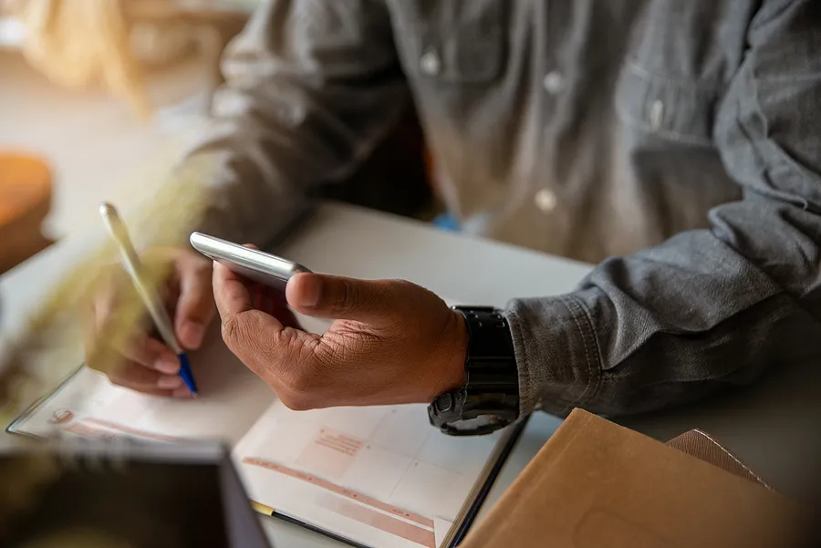 Person holding cell phone while writing in calendar.