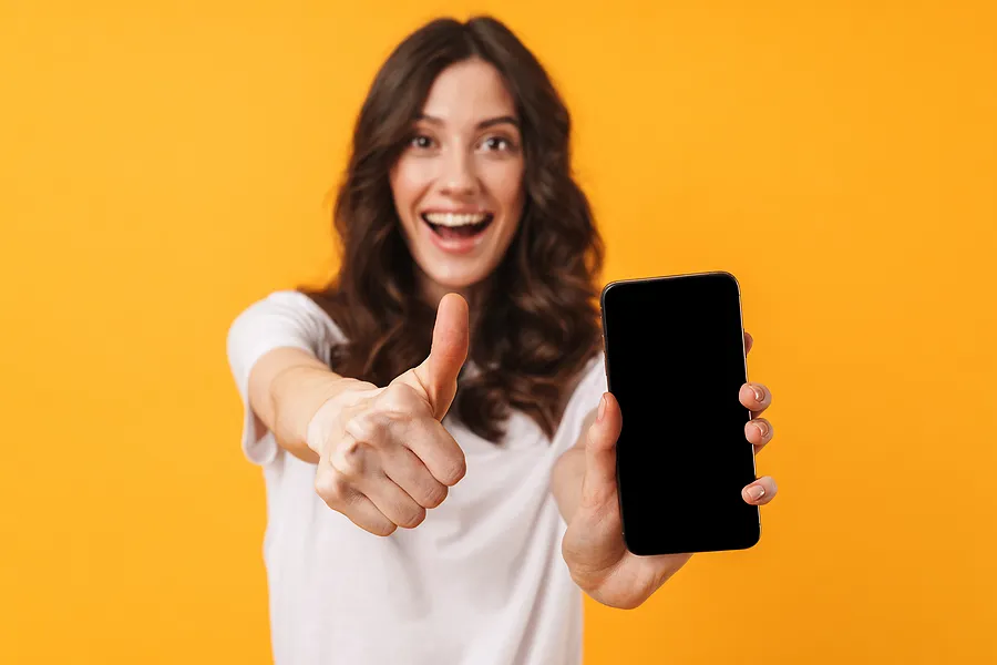 Smiling woman holding a smartphone and giving a thumbs up, symbolizing successful phone verification and certification process.