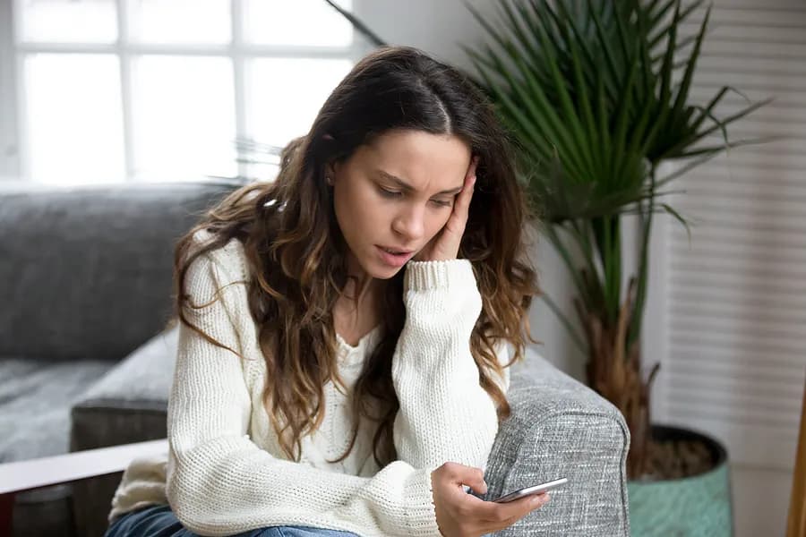 Concerned woman looking at her smartphone, representing the importance of reviewing used phone reports and understanding a device history report before buying.
