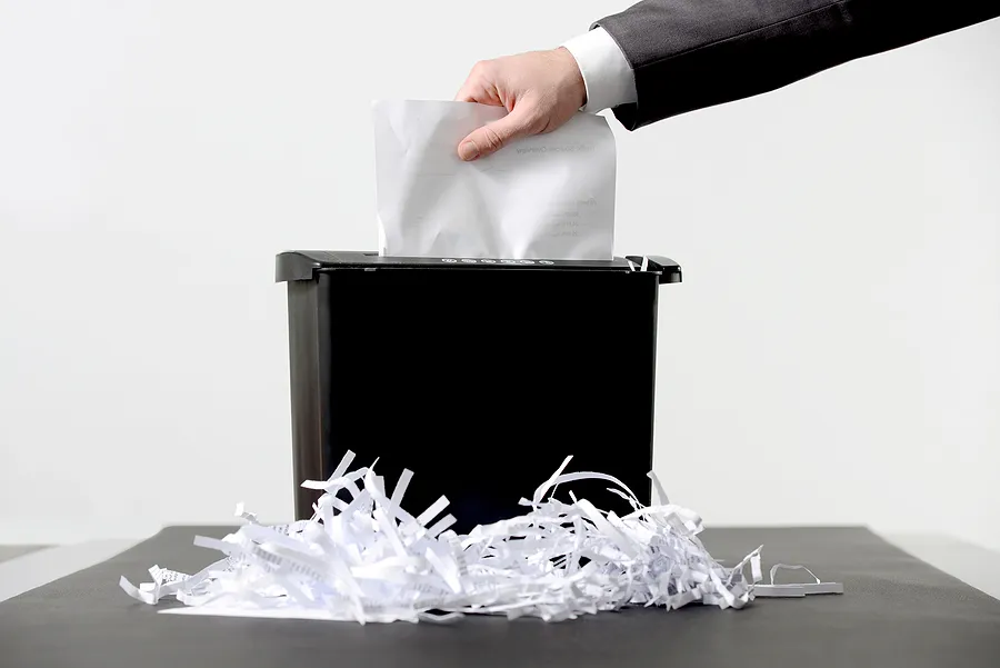 Hand placing documents into a paper shredder, illustrating certified data destruction and secure disposal of sensitive information.