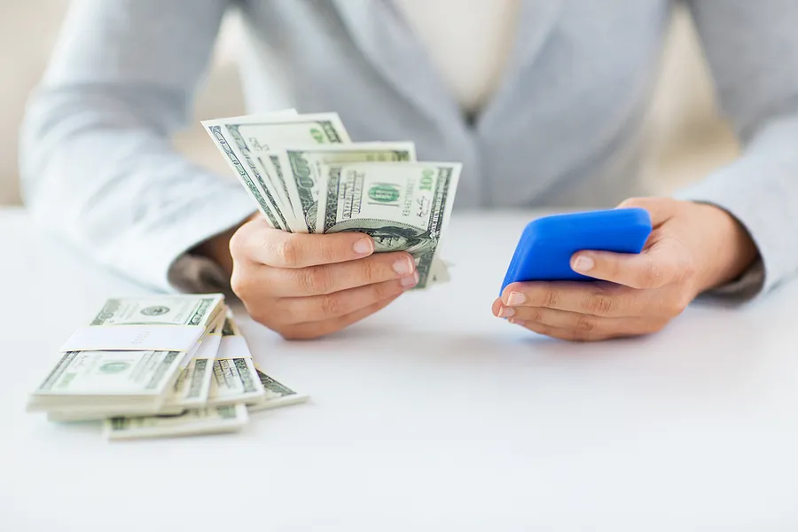 Person holding a smartphone in one hand and cash in the other, representing phone resale value and selling a used phone for money.